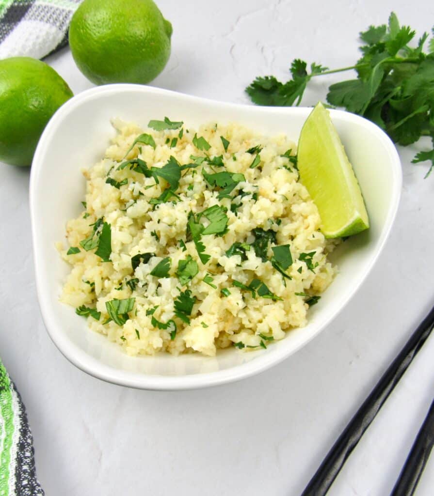 Lime cilantro cauliflower rice in white bowl with lime wedge and limes in background