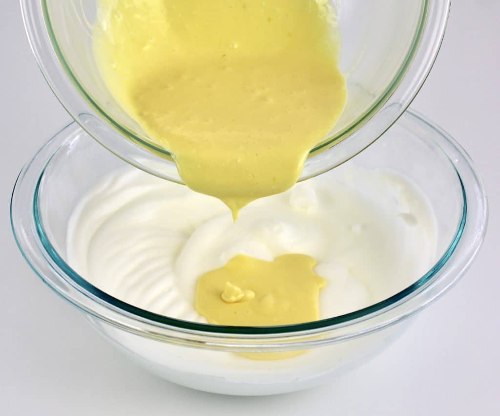 whipped egg yolks in glass bowl pouring to whipped egg whites in glass bowl