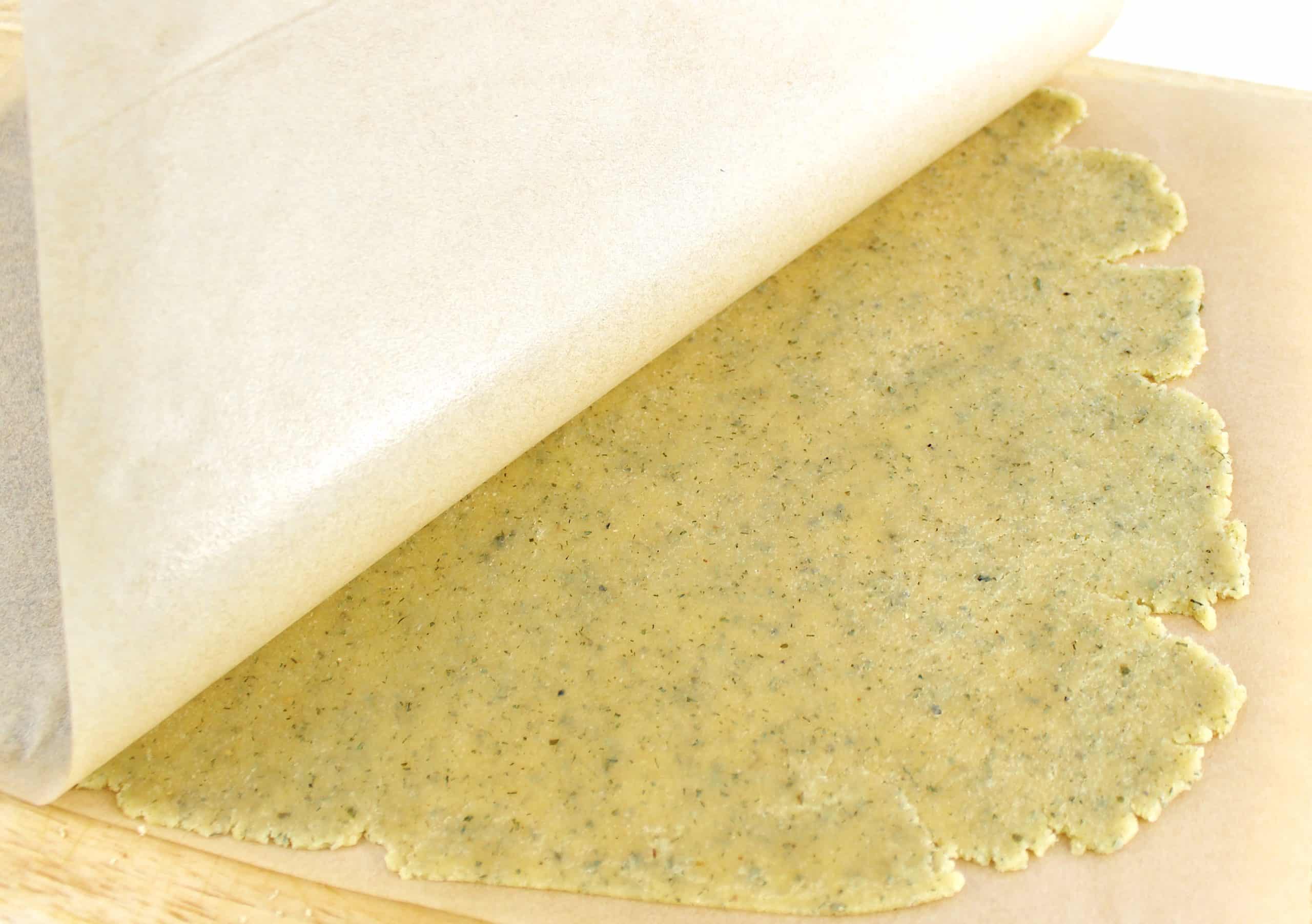 ranch cracker dough rolled out with parchment paper being lifted up