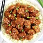 closeup of orange chicken over cauliflower rice with scallions on top