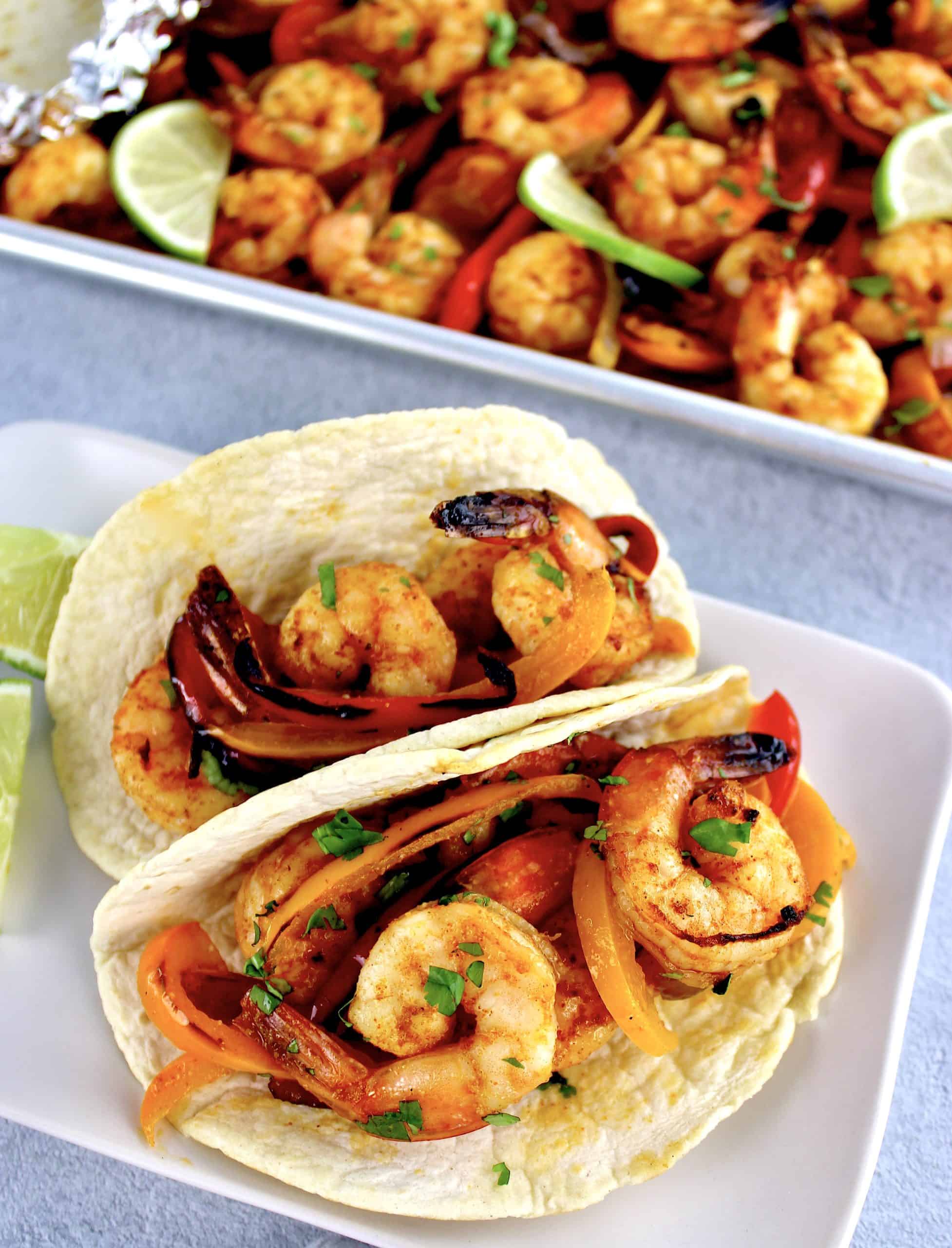shrimp fajitas in 2 tortillas on plate with baking sheet in background