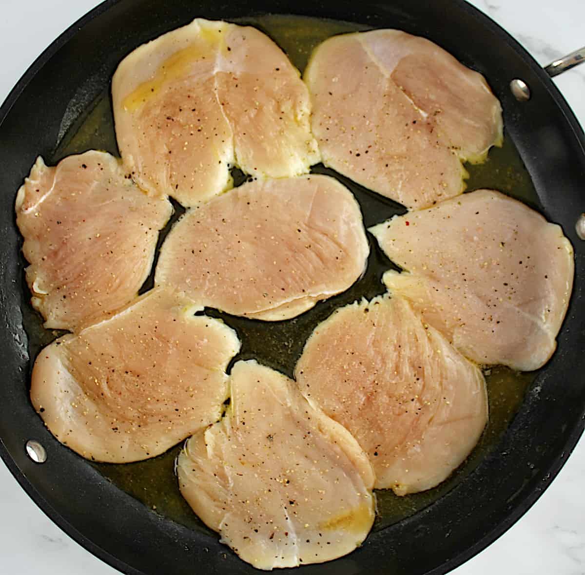 8 pieces of raw chicken cooking in skillet