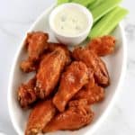 Crispy Air Fryer Buffalo Wings on white plate with bowl of blue cheese dressing and celery sticks